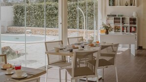 A dining area with a table set for four, overlooking a pool and garden. - Villa Patrizia Salento B&B (Porto Cesareo)