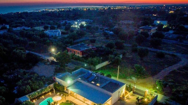 A modern house with a swimming pool, surrounded by greenery and a view of the sea at dusk. - Villa Patrizia Salento B&B (Porto Cesareo)