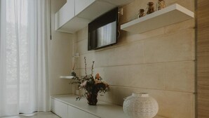 A modern living room with a flat-screen TV mounted on a wall, a console table with decorative items, and a large vase. - Villa Patrizia Salento B&B (Porto Cesareo)