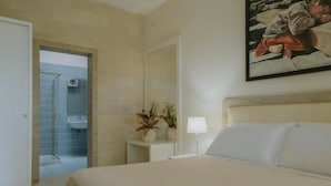 A hotel room with a bed, a bedside table with a lamp, a potted plant, and a painting on the wall. - Villa Patrizia Salento B&B (Porto Cesareo)