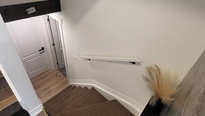 A staircase with a brown carpet, white walls, and a black shelf with a decorative plant.