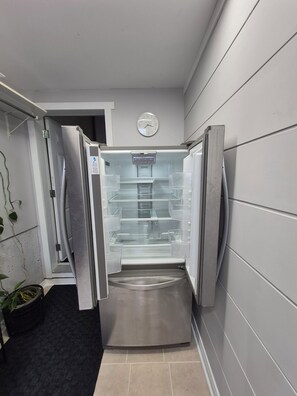 A modern kitchen with a stainless steel refrigerator, a clock on the wall, and a potted plant. - Private 2-brdm basement unit (full bathroomlaundry) (Gatineau)