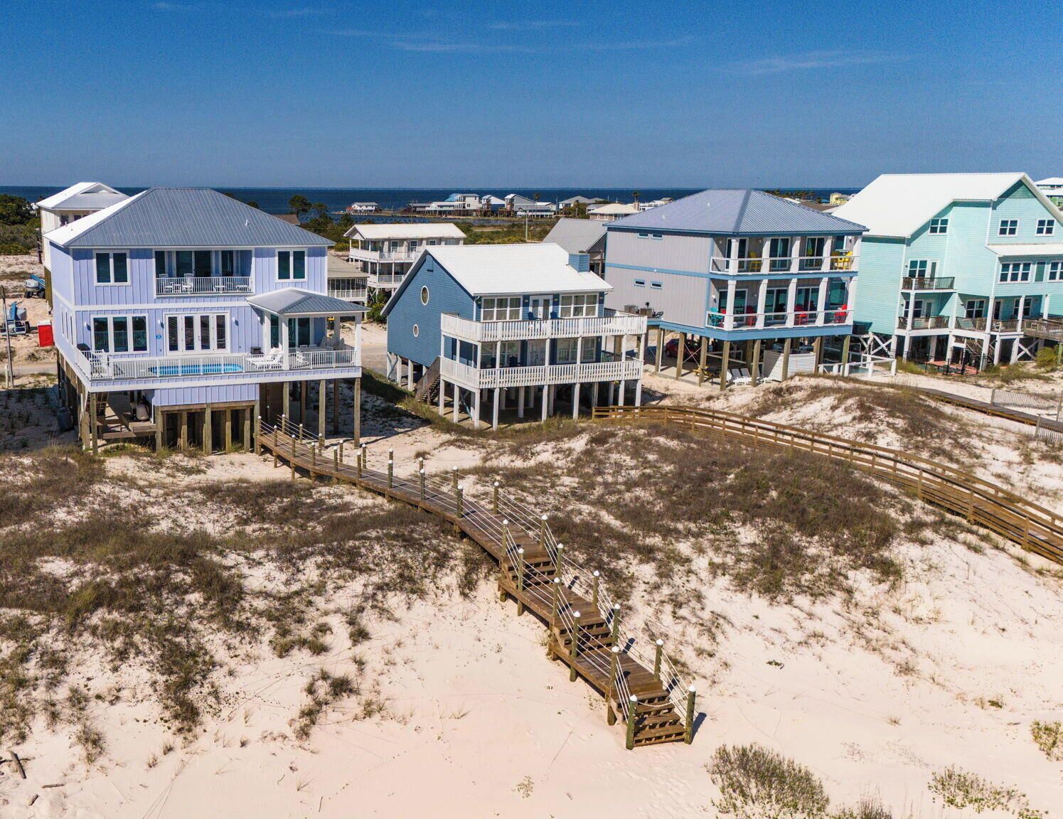 Une propriété située sur la côte, comprenant plusieurs maisons donnant sur la plage, une promenade en bois et une vue dégagée sur l’océan.