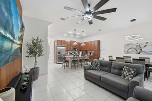 A modern kitchen with wooden cabinets, a central island, and a dining area with a gray sofa and chairs. - Tranquil Times Townhouse 4 bed Private Pool (Davenport)