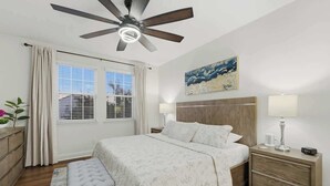 A bedroom with a bed, bedside tables, a ceiling fan, a window with curtains, a nightstand, and a painting on the wall. - Tranquil Times Townhouse 4 bed Private Pool (Davenport)