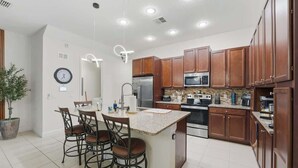 A modern kitchen with wooden cabinets, stainless steel appliances, and a central island with bar stools. - Tranquil Times Townhouse 4 bed Private Pool (Davenport)