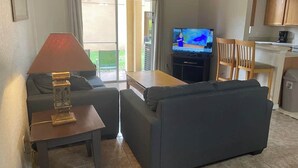 A living room with a sofa, a small table with a lamp, a TV, and a kitchen area in the background. - Regal Palms 4bd Resort Tiki Bar (Davenport)