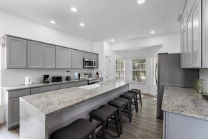 A modern kitchen with a large island, grey cabinets, stainless steel appliances, and a bar stool seating area. - Make Memories in This 6 Bedroom With Private Pool (Davenport)