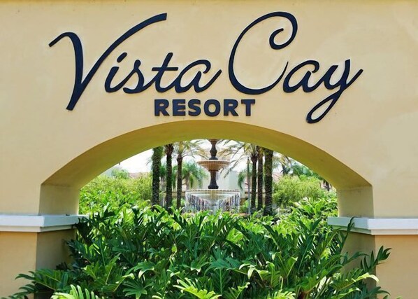Indgangen til Vista Cay Resort med en buegang, frodig beplantning og en fontæne i baggrunden.