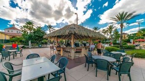 An outdoor patio area with tables and chairs, a thatched-roof bar, and palm trees. - Cute 3bd 2 5bth Amazing Resort (Davenport)