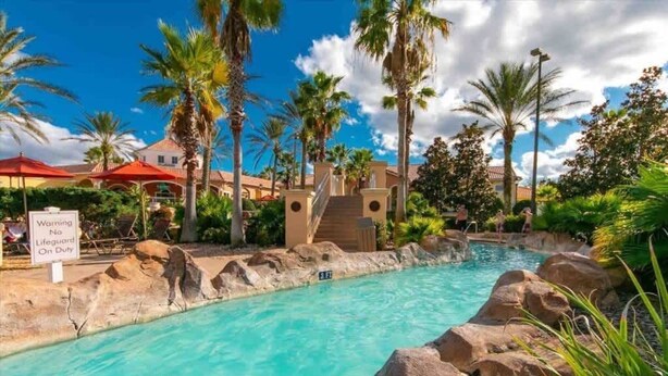 A pool area with clear water, palm trees, and a lifeguard on duty sign. - Cute 3bd 2 5bth Amazing Resort (Davenport)