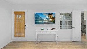 Um quarto com porta branca, um console branco e uma televisão de tela plana, além de uma janela com persianas.