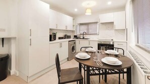 A modern kitchen with white cabinets, a built-in washing machine, and a dining area with a table set for four. - 3bed House - Close to Worksop Mansfield (Mansfield)