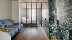 A modern bedroom with a grey sofa, a bed with white linens, and a glass partition. - w Dreamy 1BR w Private Terrace Skyline View (Milan)