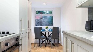 Eine kleine Küche mit weißen Schränken, einer zentralen Kochinsel mit Spüle und einem Fenster mit Gartenblick.