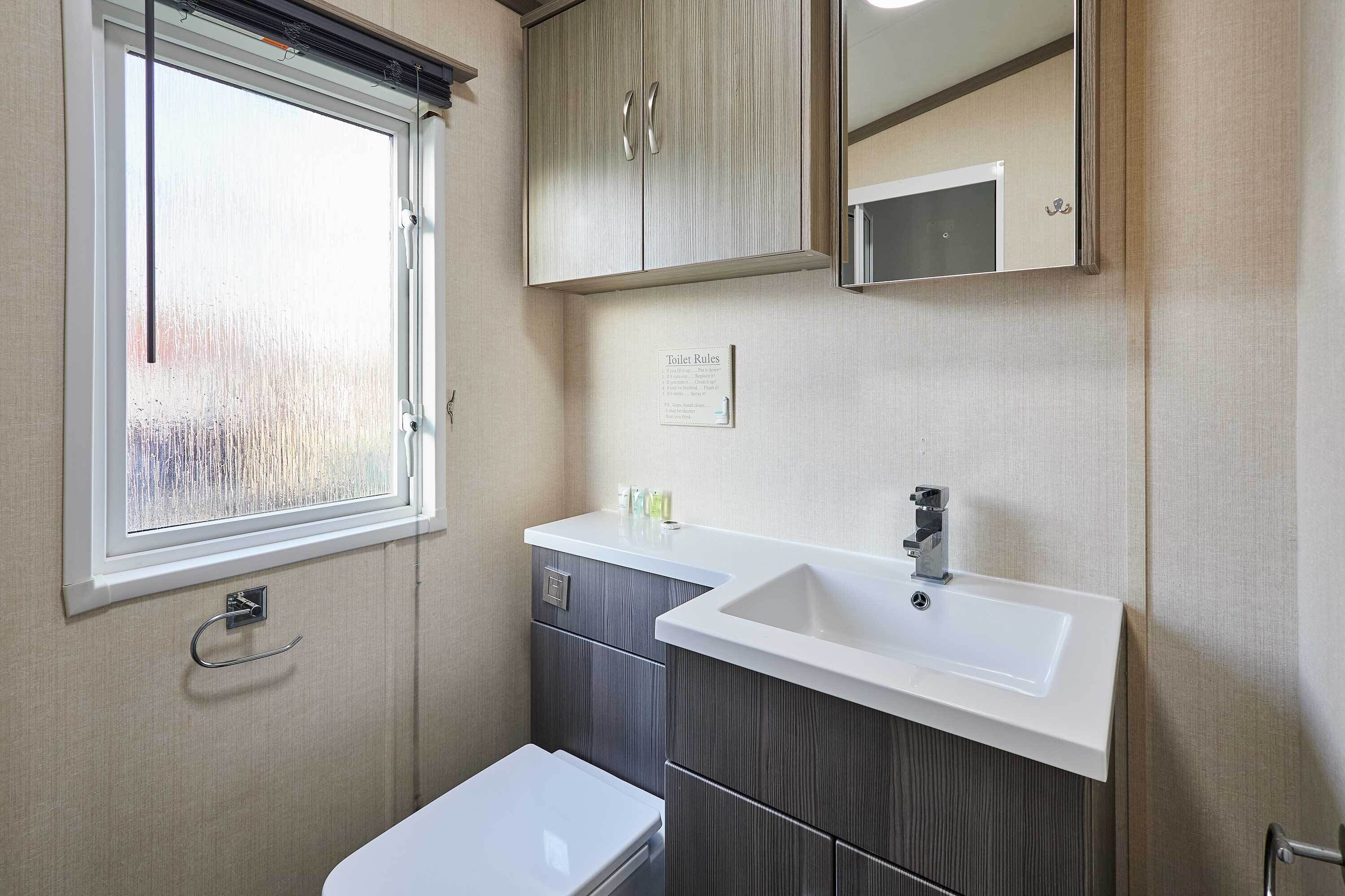 A compact bathroom with a white sink, a mirror, and a window with blinds.