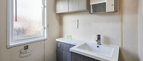 A compact bathroom with a white sink, a mirror, and a window with blinds.