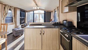 A modern kitchen with wooden cabinets, a gas stove, and a dining area with a table and chairs. - Host Stay 10th Avenue (Morpeth)