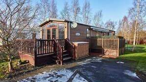 A small, single-story mobile home with a deck, a fenced area, and a snow-covered ground. - Host Stay 10th Avenue (Morpeth)