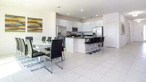 Una cocina moderna con armarios blancos, una isla central y un comedor con mesa y sillas.