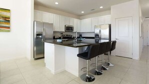 Una cocina moderna con armarios blancos, electrodomésticos de acero inoxidable y una isla central con taburetes de bar.