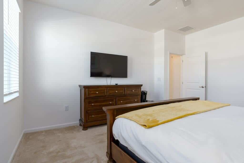 A bedroom with a bed, a dresser, a television, and a door.