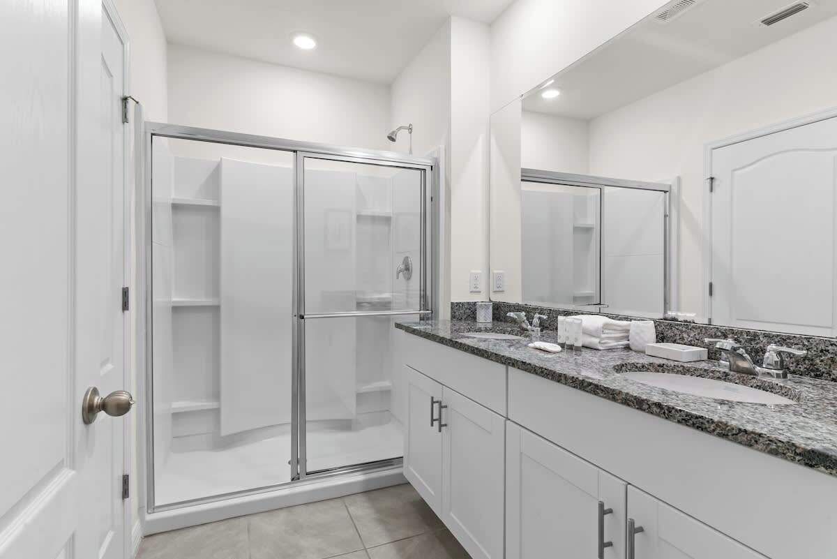 Une salle de bain moderne avec une douche à parois de verre, un grand miroir et un lavabo encastré dans un plan de travail en granit.