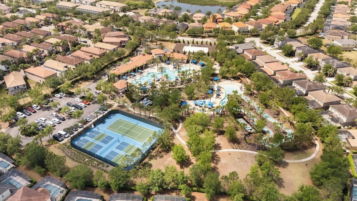Vue aérienne d’un quartier résidentiel avec une grande piscine, des courts de tennis et un parc aquatique.