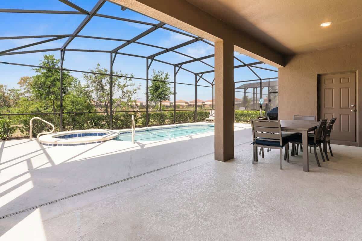 A covered outdoor area with a pool, a dining table, and chairs.