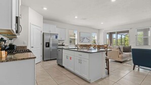 A modern kitchen with white cabinetry, a central island, and a dining area with a blue chair. - Beautiful 6br5bathpool Clubhouse (Davenport)