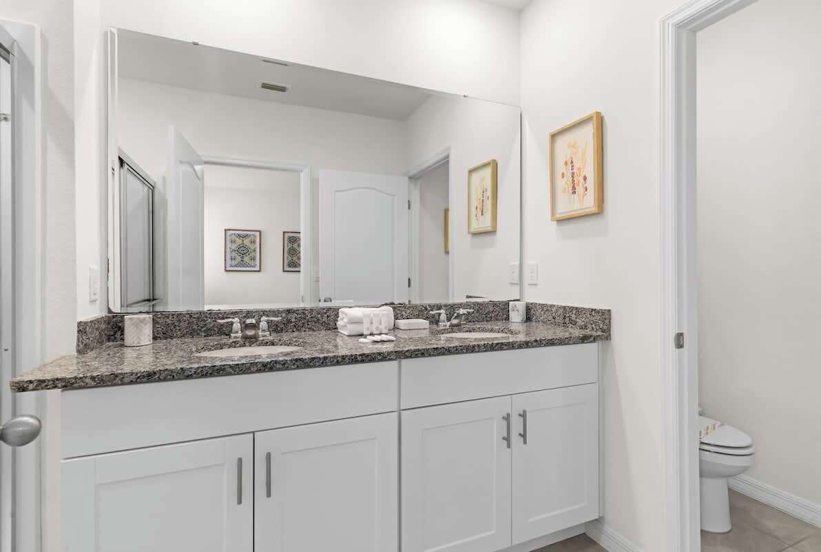 Un baño moderno con lavamanos doble, muebles blancos y un espejo grande.