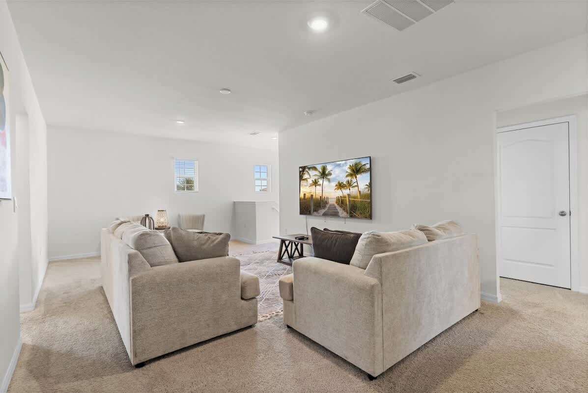 A spacious living room with two beige sofas, a coffee table, and a painting of a sunset on the wall.