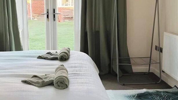 A hotel room with a bed, a metal drying rack, and a view of a building through a window with curtains. - 1-bed Hideout in Ripon With Free Parking (Ripon)