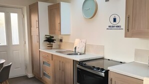 A modern kitchen with wooden cabinets, a sink, an oven, and a clock on the wall. - 1-bed Hideout in Ripon With Free Parking (Ripon)