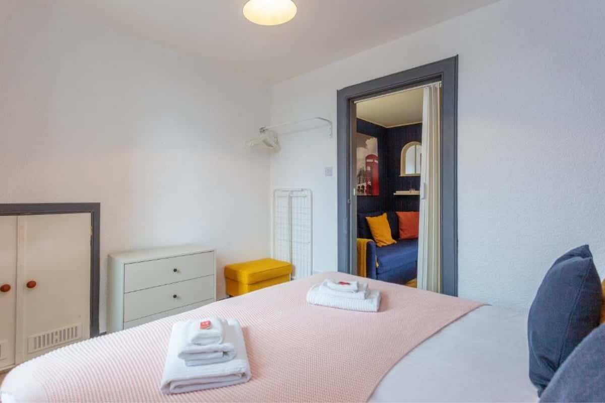 A hotel room with a bed, a white wardrobe, a yellow bench, and a door leading to another room.