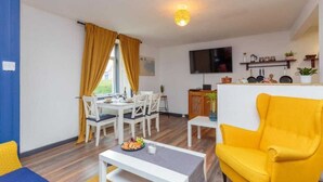 A compact living space with a dining area, a yellow armchair, a flat-screen TV, and a kitchen counter. - 1 Bedroom Scottish Cottage-on Street Parking (Selkirk)