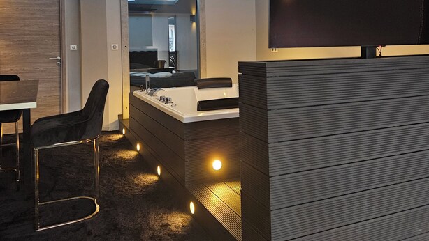 A modern interior with a dark carpet, a wooden desk, a black chair, and a large mirror. - Love Room Le Jardin D'Éden (La Motte-Servolex)