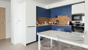 Eine moderne Küche mit weißen und blauen Schränken, einer weißen Arbeitsplatte und einem Glastisch mit Stühlen.