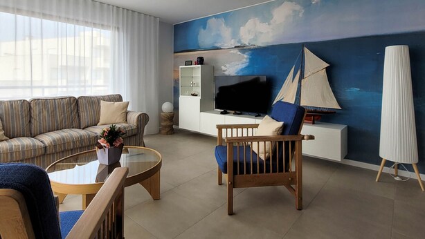 Ein modernes Wohnzimmer mit einer Couch, einem Couchtisch, einem Fernseher und einem Wandgemälde mit einem Segelboot.