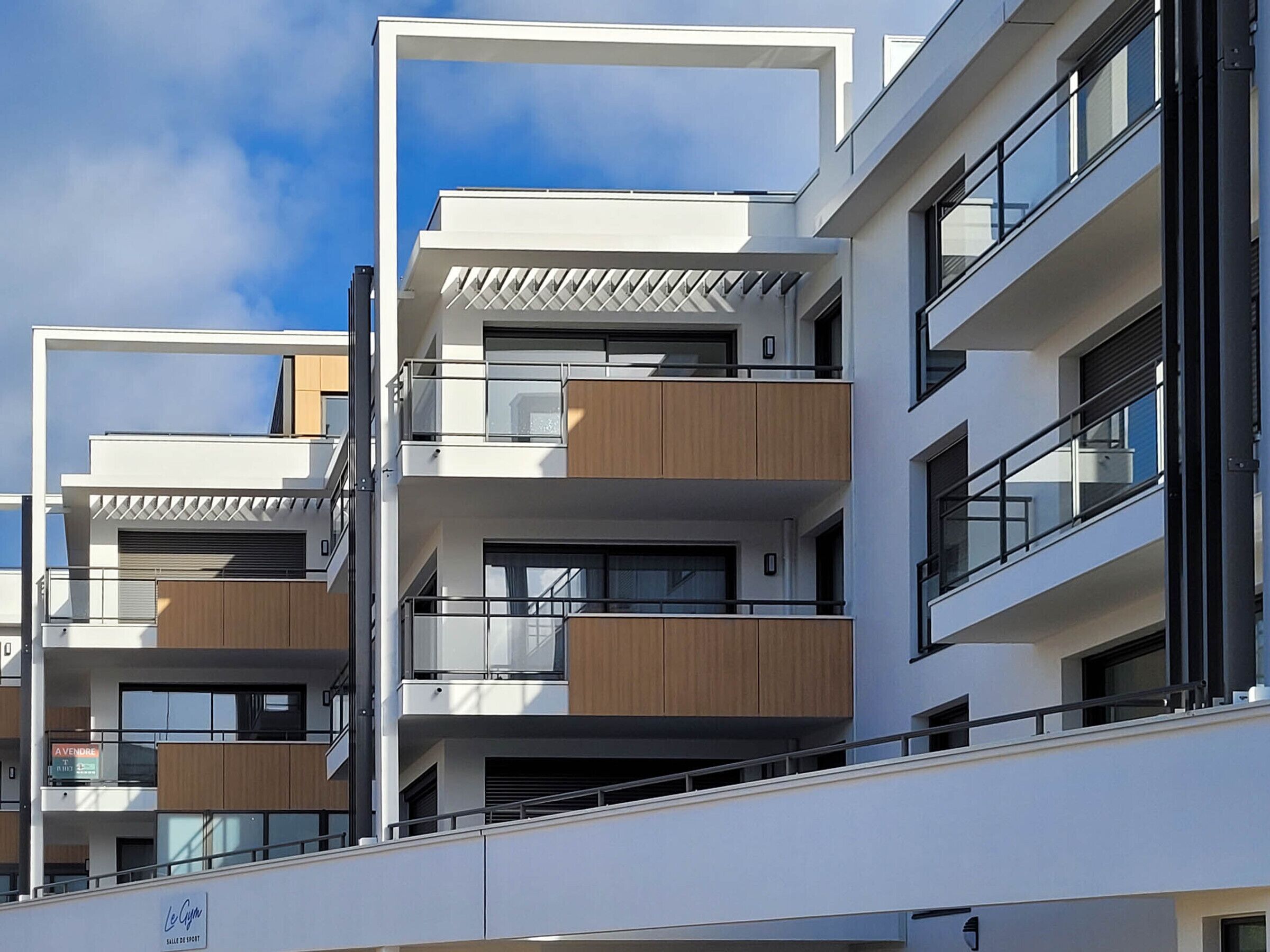 A modern multi-story building with balconies, large windows, and a clear sky.