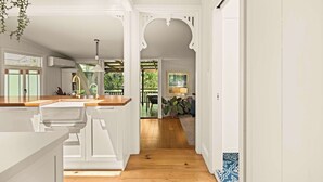 A spacious hallway with wooden flooring, white walls, and a view of an outdoor deck with plants. - 1920s Cottage Near Paddington and CBD (Bardon)