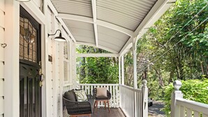 A covered porch with a wooden floor, two chairs, a bench, and a white railing. - 1920s Cottage Near Paddington and CBD (Bardon)