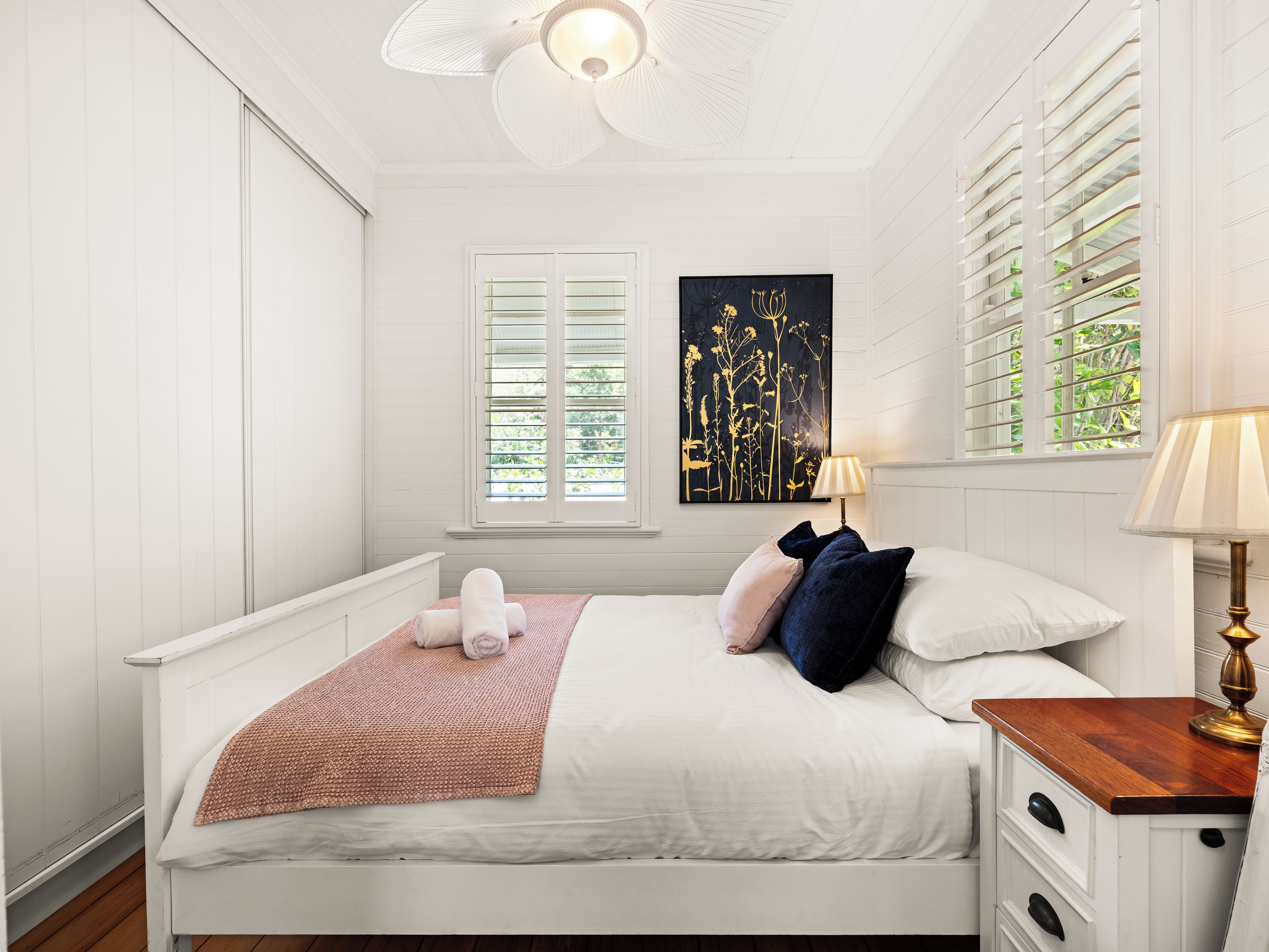 Un dormitorio con cama, mesita de noche, lámpara y ventana con persianas.