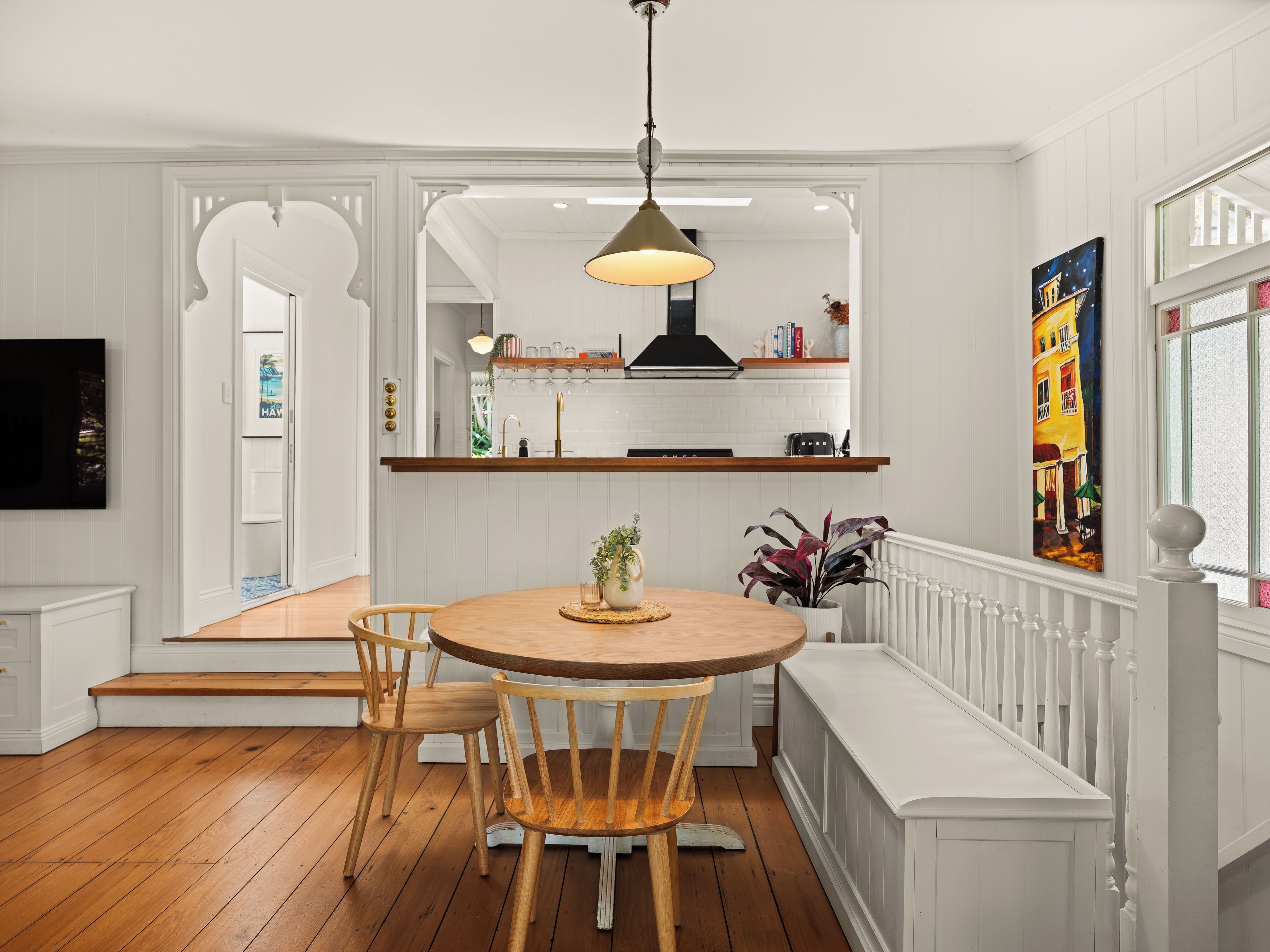 A kitchen with white cabinetry, a wooden dining table, and a hanging pendant light.