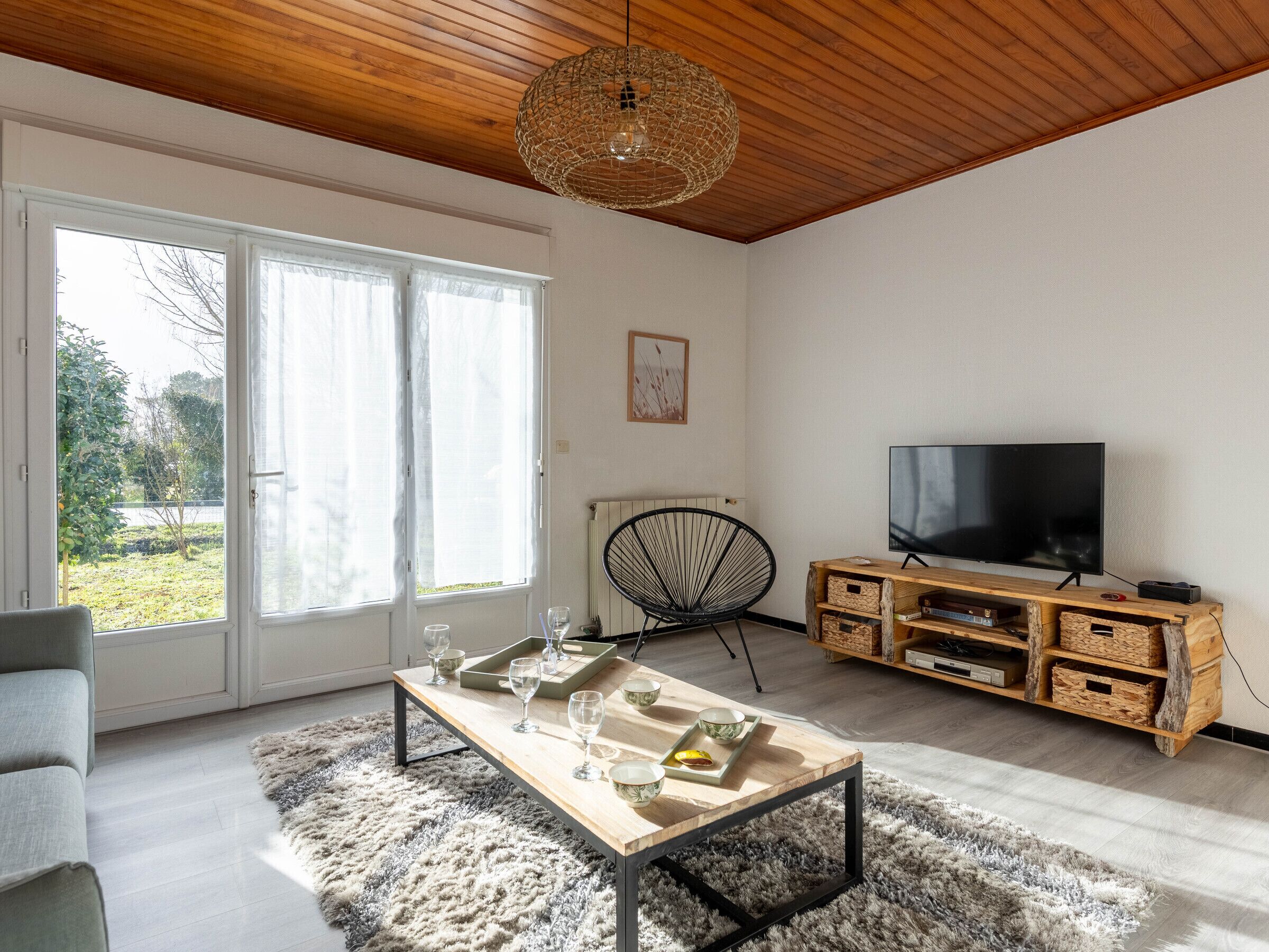 Una sala de estar moderna con techo de madera, un televisor grande, una mesa de comedor con vasos y recipientes, y una silla.