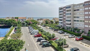 Una calle residencial con coches aparcados, una piscina y edificios con balcones que dan a la calle.
