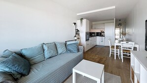Una sala de estar moderna con un sofá gris, una mesa de centro blanca y una cocina al fondo.