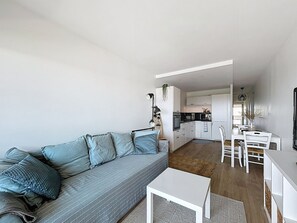 A modern living room with a grey sofa, white coffee table, and a kitchen in the background. - Sea View Apartment with Terrace & Parking (Mauguio)