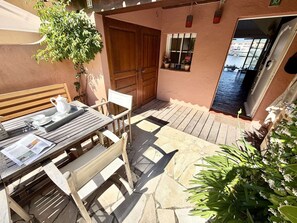 Eine Terrasse mit Holztisch, gedeckt für zwei Personen, einer Holzbank und einem Blumentopf.