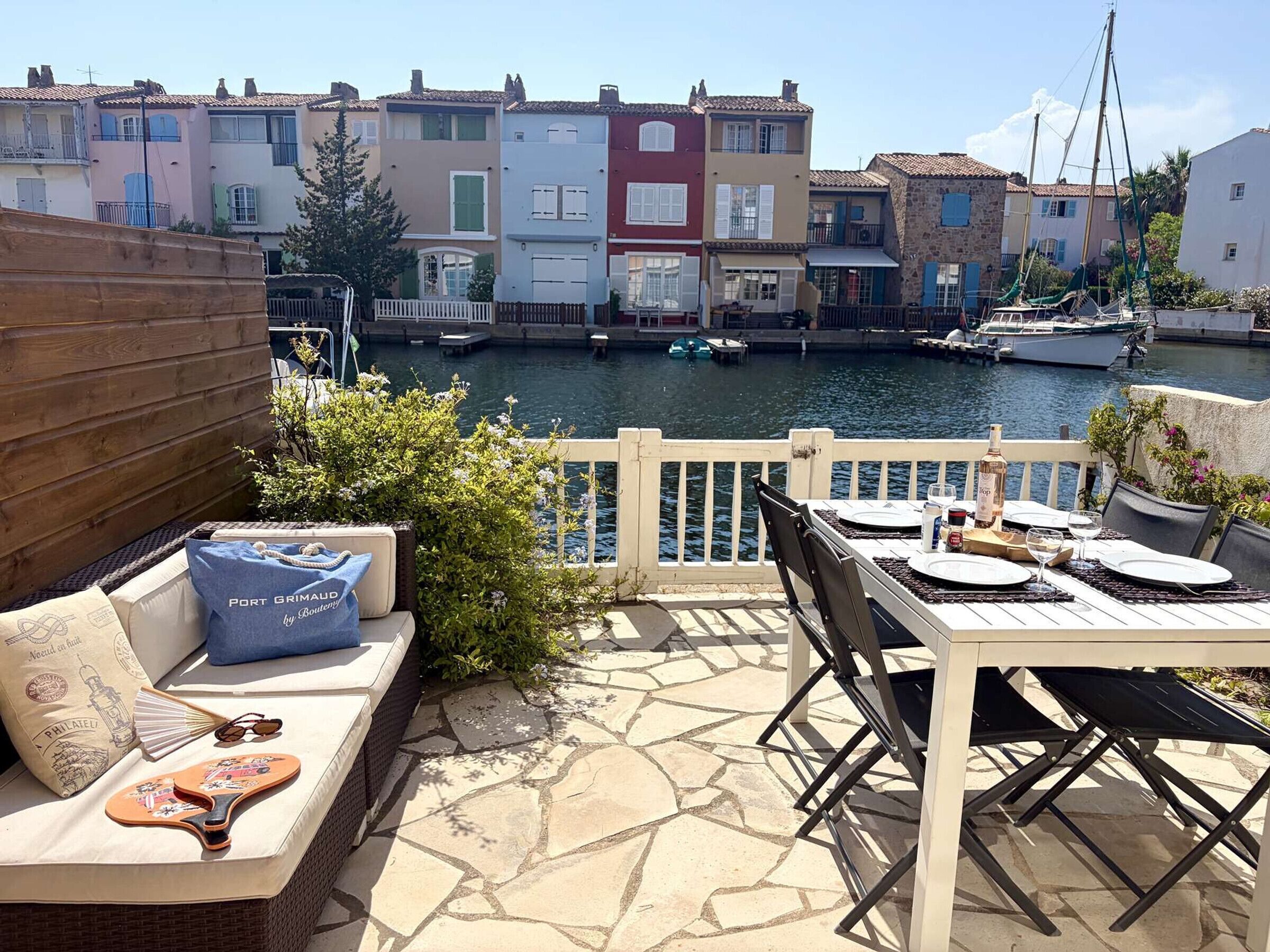 Terraço com mesa posta para refeições, com vista para um canal com barcos e edifícios coloridos.